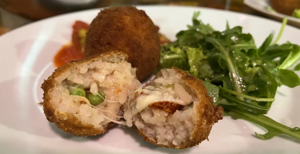 Two arancini - cut in the foreground, intact in the background - with some salad.